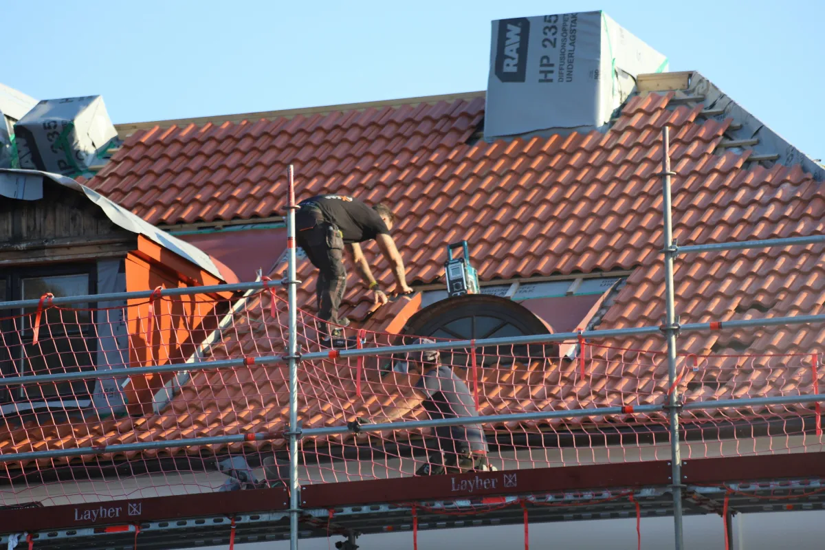 Couvreur posant une membrane d’étanchéité autour d’une cheminée sur toit en tuiles, échafaudage en place