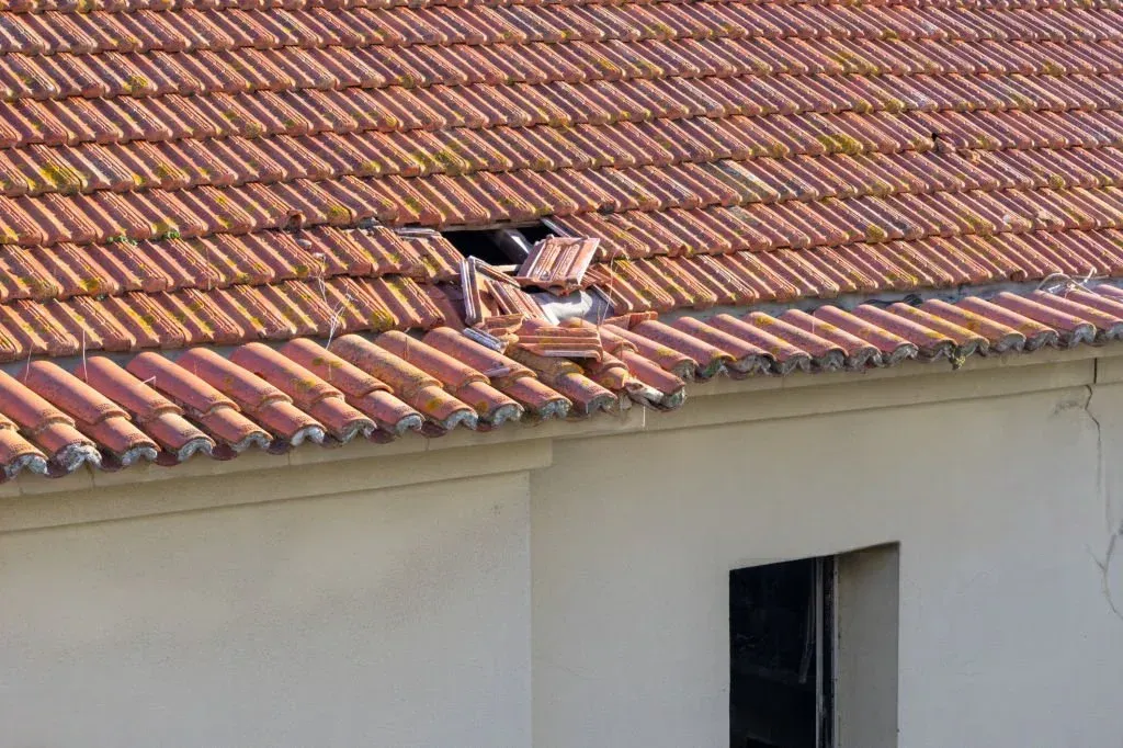 Trou béant dans une toiture en tuiles signalant une fuite à réparer en urgence