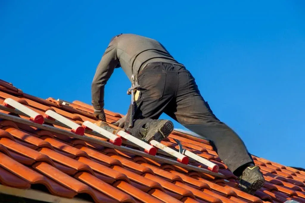 Couvreur sécurisé sur toit en tuiles rouges réalisant une rénovation partielle